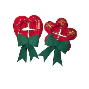 May include: Two red felt Christmas ornaments with green bows. One ornament is heart-shaped with embroidered candles and blue dots. The other is flower-shaped with gold embroidered holly leaves. Both have a white cross design.