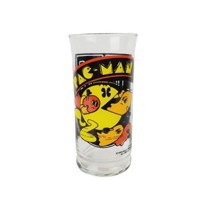 May include: A clear glass with a black and yellow Pac-Man graphic. The graphic shows Pac-Man eating a red ghost. The text "Pac-Man" is printed in black on the glass.