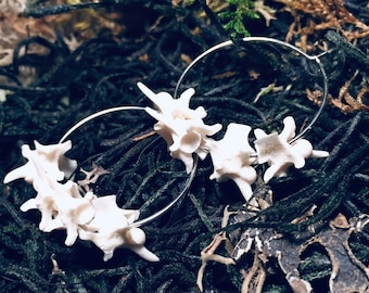 May include: A pair of hoop earrings with a silver metal hoop and a cluster of white bone-like charms. The charms are arranged in a random pattern and appear to be made of real bone.