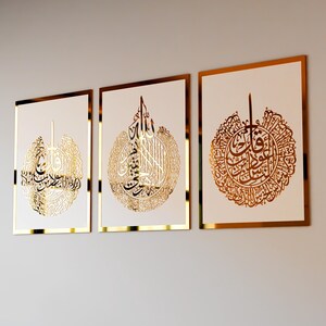 May include: Three gold framed wall art pieces with white backgrounds and intricate gold calligraphy designs. The designs are circular and feature Arabic script.