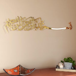 Op de afbeelding: Gouden metalen wandkunst met Arabische kalligrafie. De kalligrafie luidt "Bismillah Al-Rahman Al-Rahim", wat vertaald wordt als "In de naam van Allah, de Meest Barmhartige, de Meest Genadevolle".