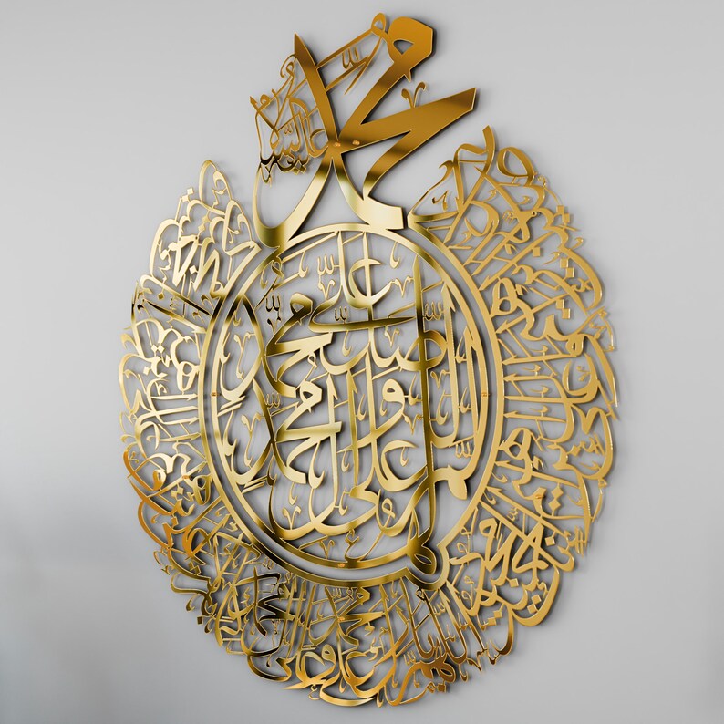 May include: A gold-colored metal wall art piece featuring intricate Arabic calligraphy in a circular design. The calligraphy is in a traditional style and is surrounded by a decorative border.