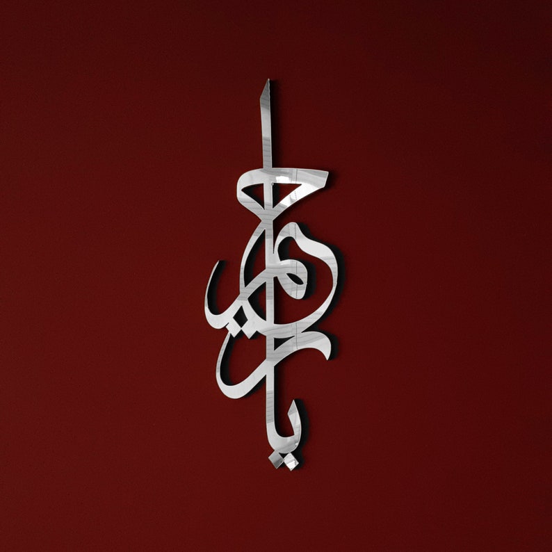 May include: A silver metallic wall decoration in the shape of Arabic calligraphy. The design is intricate and features a flowing script.