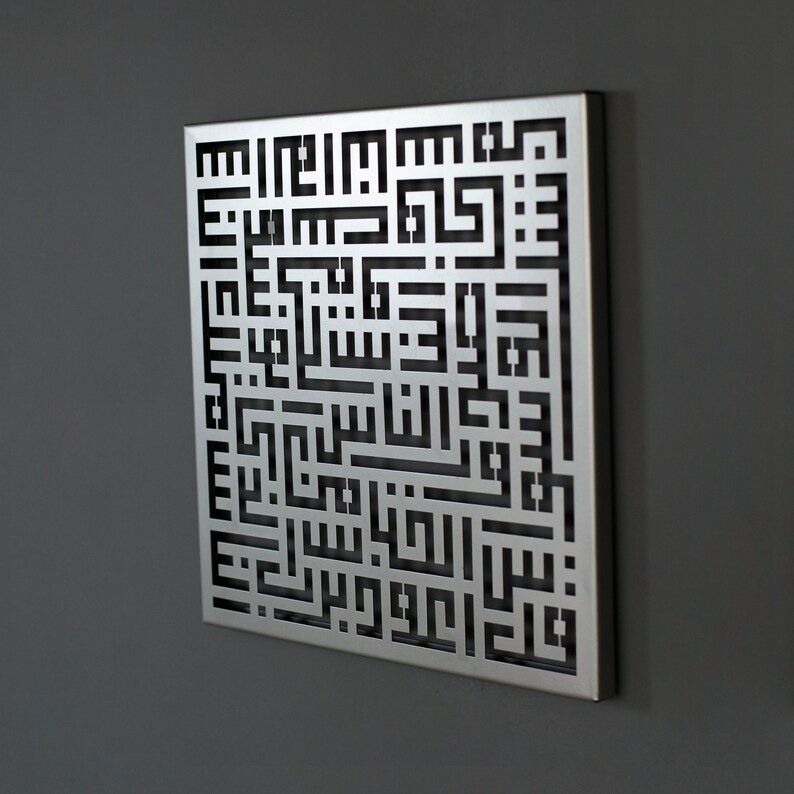 May include: A silver metal wall art piece with a black cutout design of Arabic calligraphy. The design is intricate and detailed, and the piece is a beautiful example of Islamic art.