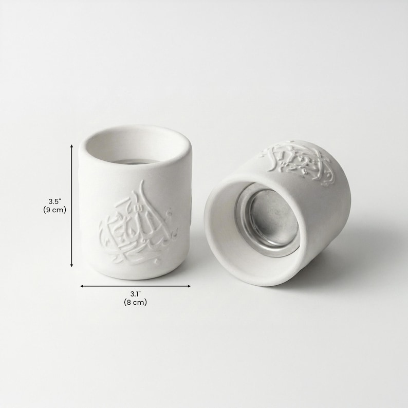 Peut inclure: Deux bougeoirs en c&eacute;ramique blanche, un debout et un sur le c&ocirc;t&eacute;. Chacun porte un motif en relief de calligraphie arabe. Le bougeoir debout mesure 9 cm de haut et 8 cm de large.