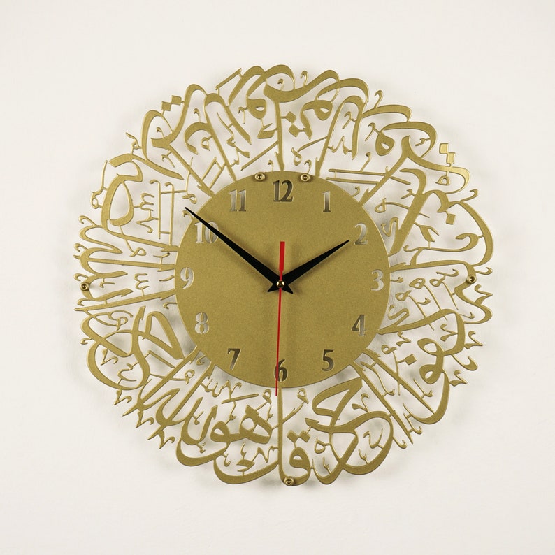 K&ouml;nnte beinhalten: Goldfarbene Wanduhr mit arabischer Kalligraphie, die das Zifferblatt umgibt. Das Zifferblatt hat schwarze Zeiger und r&ouml;mische Ziffern.
