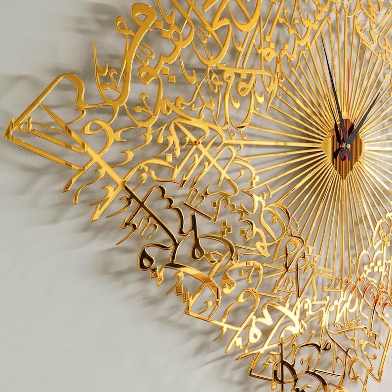 May include: A gold-colored wall clock with intricate Arabic calligraphy design. The clock features a sunburst pattern and black clock hands with a red second hand. The clock's design is a decorative piece for home decor.