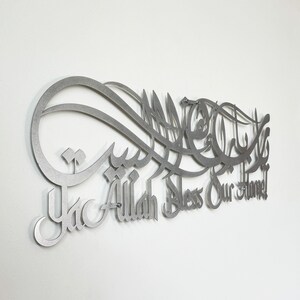 May include: A silver metal wall art piece with Arabic calligraphy and the words "Ya Allah Bless Our Home".