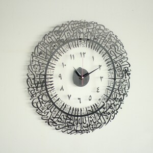 May include: A black metal clock with Arabic calligraphy around the face. The clock face is white with black numbers and hands.