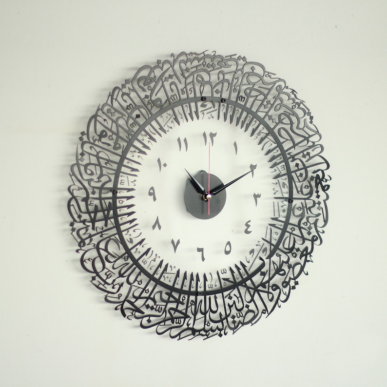 May include: A black metal clock with Arabic calligraphy around the face. The clock face is white with black numbers and hands.