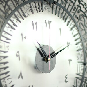 May include: A black and white clock with Arabic numerals. The clock face is white with black numbers and hands. The clock is framed in black metal with Arabic script.