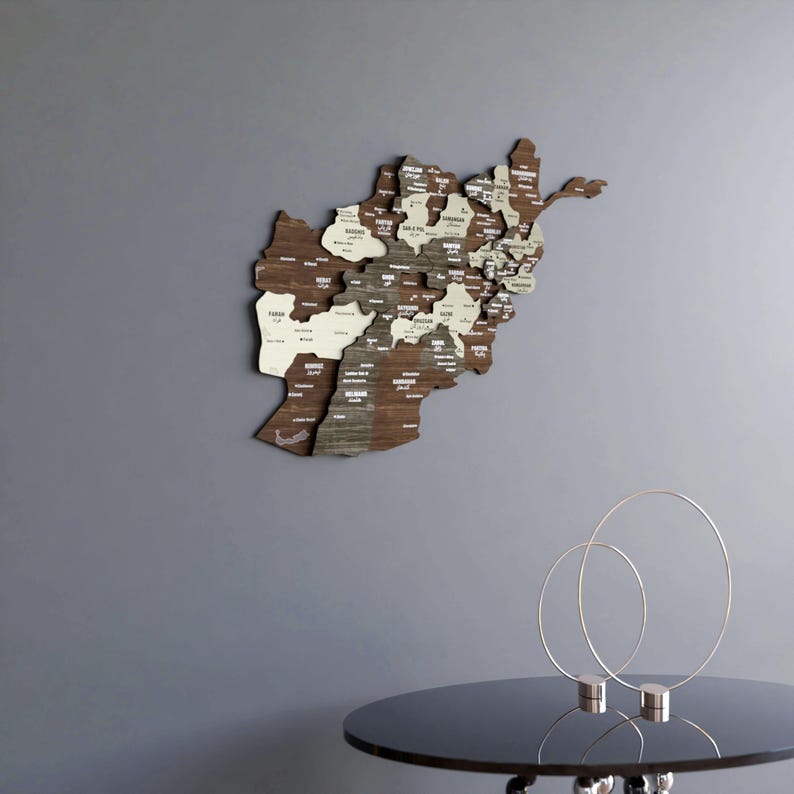 May include: A wooden map of Afghanistan with the names of each province printed on it. The map is mounted on a gray wall and is surrounded by a white border. The map is a decorative piece of art that would be perfect for a home office or living room.