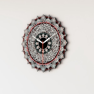 Op de afbeelding: Een ronde wandklok met Arabische kalligrafie en ingewikkelde ontwerpen in rood, blauw en groen. De wijzerplaat van de klok is zwart met witte cijfers en wijzers.