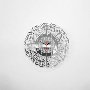 May include: A silver mirrored clock with Arabic calligraphy around the face. The clock face has black hands and black numbers.