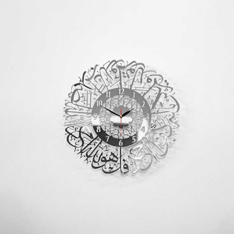 May include: A silver mirrored clock with Arabic calligraphy around the face. The clock face has black hands and black numbers.
