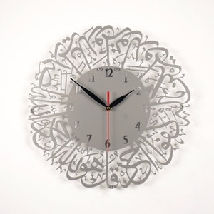 K&ouml;nnte beinhalten: Eine graue Wanduhr aus Metall mit arabischer Kalligraphie um das Zifferblatt. Die Uhr hat schwarze Zeiger und einen roten Sekundenzeiger. Die Zahlen auf dem Zifferblatt sind schwarz.