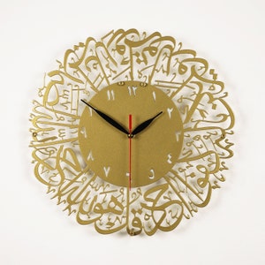 K&ouml;nnte beinhalten: Goldfarbene Wanduhr mit arabischer Kalligraphie um das Zifferblatt. Das Zifferblatt hat schwarze Zeiger und wei&szlig;e r&ouml;mische Ziffern.