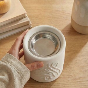Peut inclure: Un diffuseur d'huiles essentielles en c&eacute;ramique blanche avec un r&eacute;cipient en m&eacute;tal argent&eacute;. Le diffuseur a une forme cylindrique avec un motif en relief. Un objet de d&eacute;coration pour l'aromath&eacute;rapie.
