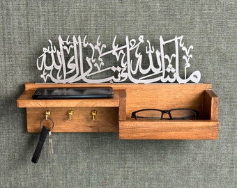 May include: A wooden wall-mounted key holder with a shelf for a phone or glasses. It has three hooks for keys and a small shelf for glasses. The key holder is decorated with a silver metal inscription that reads "Allah" in Arabic calligraphy.