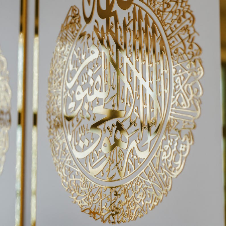 May include: A gold-colored metal wall decor featuring intricate Arabic calligraphy in a circular design.