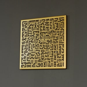 May include: A gold-colored metal wall art piece with a geometric design featuring intricate black lines. The design is reminiscent of Arabic calligraphy.