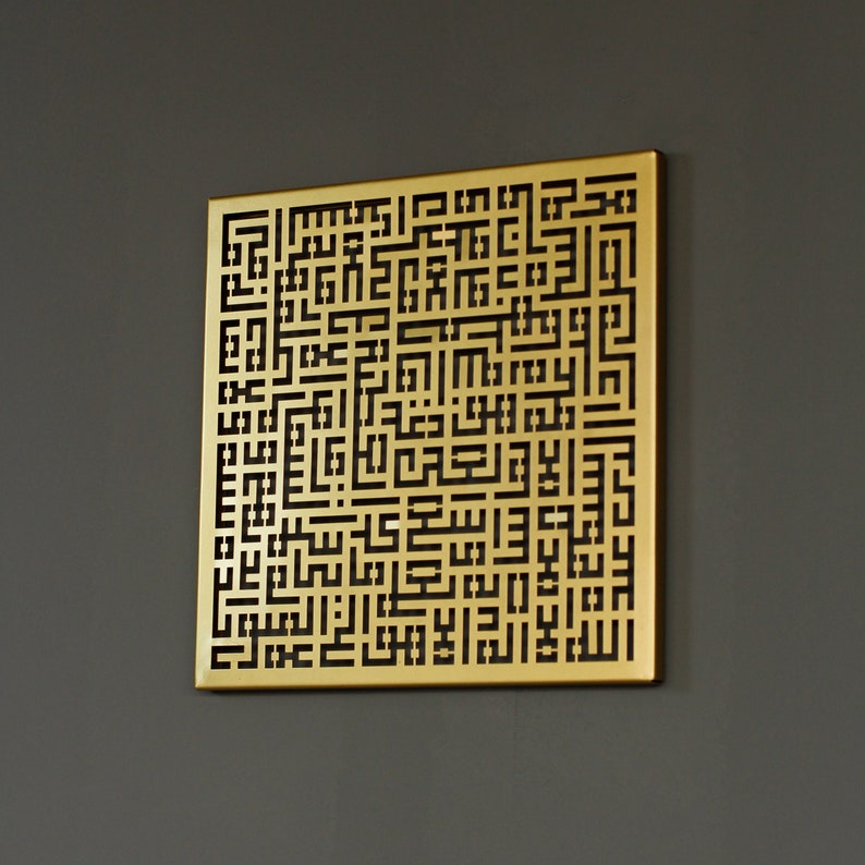 May include: A gold-colored metal wall art piece with a geometric design featuring intricate black lines. The design is reminiscent of Arabic calligraphy.