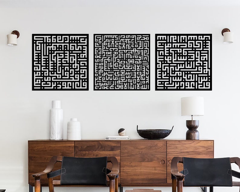May include: Three black and white square wall art pieces with intricate Arabic calligraphy designs. The art is displayed on a white wall above a wooden dresser with two chairs.