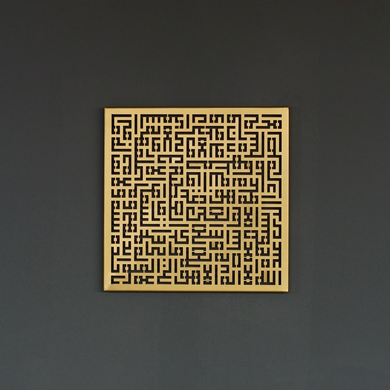 May include: A gold-colored metal wall art piece with a geometric design featuring black Arabic calligraphy.