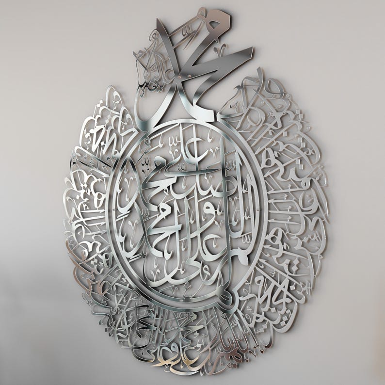 May include: A silver metal wall art featuring intricate Arabic calligraphy in a circular design. The calligraphy is in a traditional style and is surrounded by a decorative border.