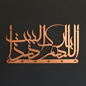 K&ouml;nnte beinhalten: Eine kupferfarbene Wanddekoration aus Metall mit arabischer Kalligraphie. Das Design ist filigran und detailliert, mit einer flie&szlig;enden Schrift, die ein Gef&uuml;hl von Bewegung erzeugt. Das St&uuml;ck ist auf einem schwarzen Hintergrund montiert.