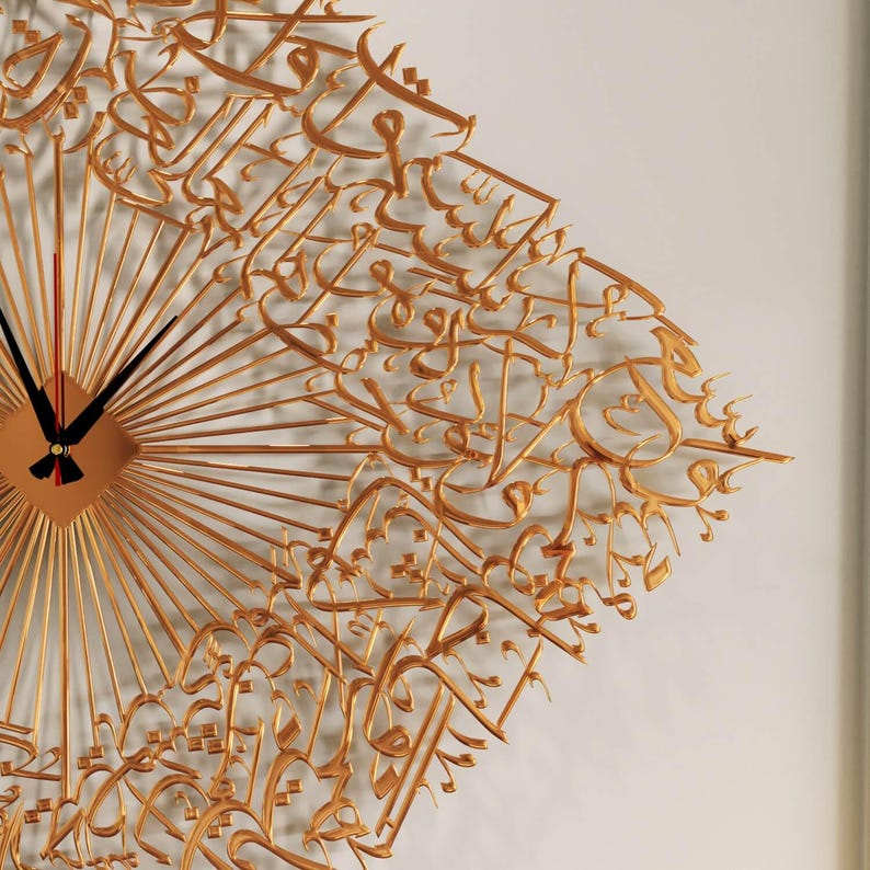 May include: Gold-colored wall clock with a unique design. The clock features a square center with radiating lines and black clock hands. Intricate gold calligraphy covers the clock face, adding an artistic touch to the decor.