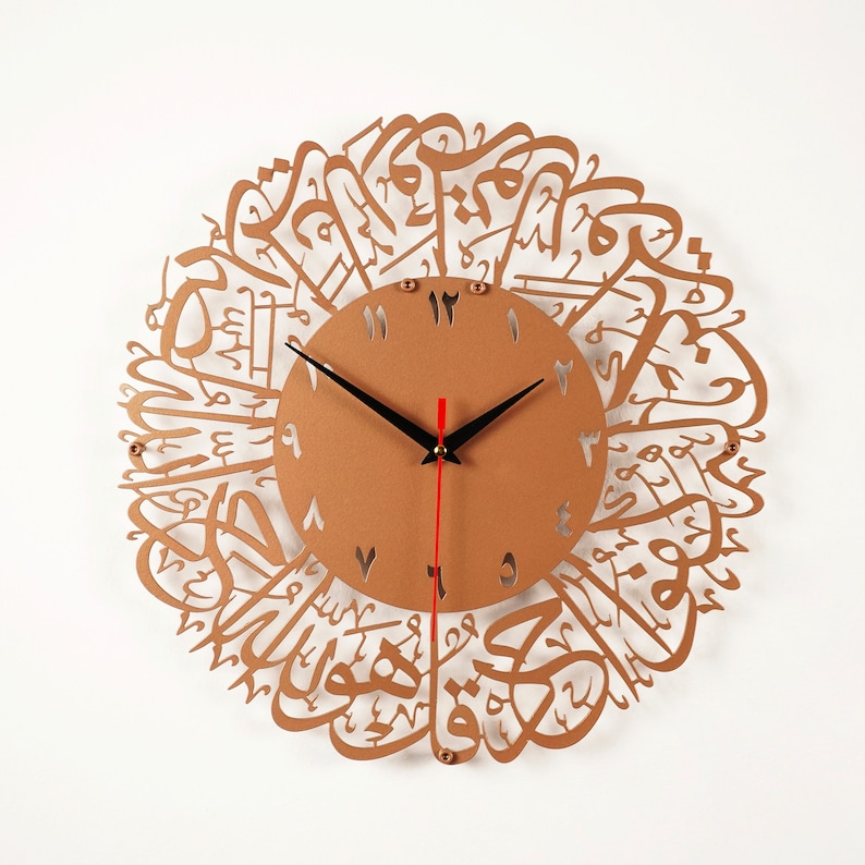 K&ouml;nnte beinhalten: Eine goldfarbene Wanduhr mit arabischer Kalligraphie um das Zifferblatt. Die Uhr hat schwarze Zeiger und einen roten Sekundenzeiger.