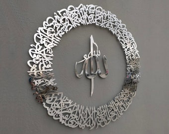 May include: A silver metal wall decor featuring an intricate circular design of Arabic calligraphy surrounding the word "Allah" in the center.
