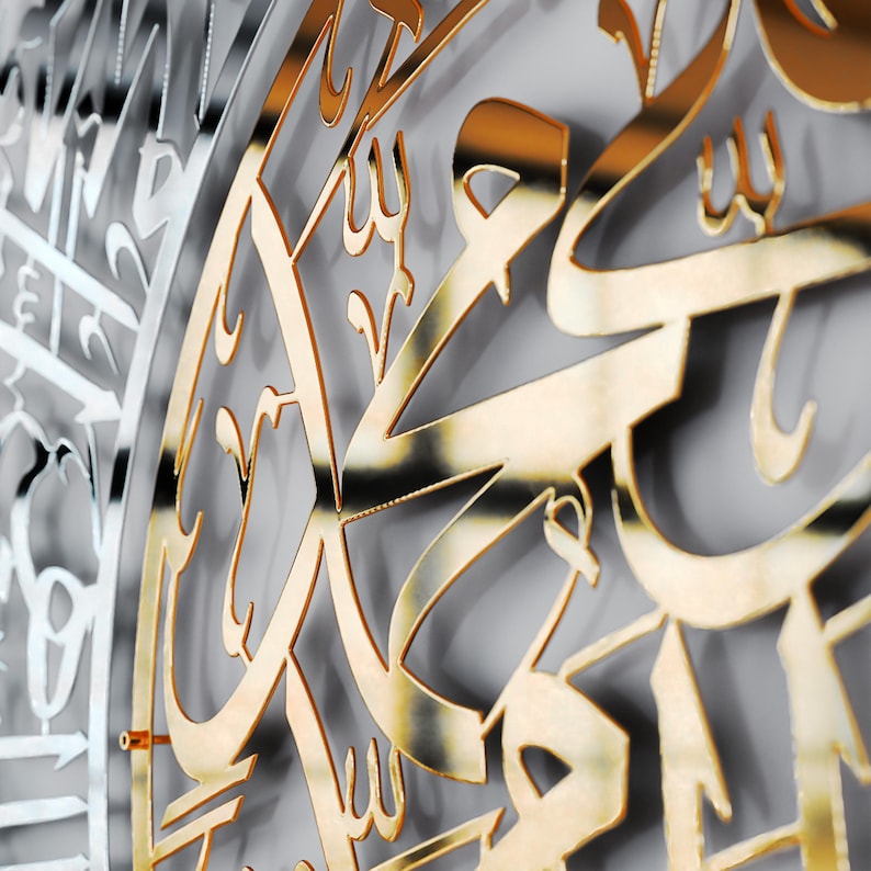 May include: A close-up of a gold-colored metal wall art piece with intricate Arabic calligraphy. The design is circular and features a repeating pattern of stylized letters.