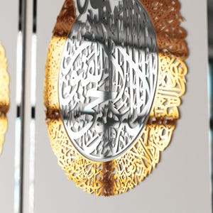 May include: A circular wall decor with intricate gold and silver Arabic calligraphy. The design features a central circle with silver calligraphy surrounded by a gold border with more calligraphy.