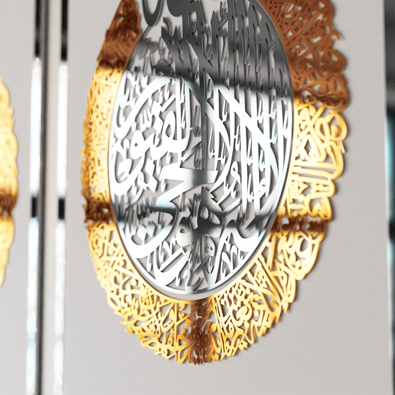 May include: A circular wall decor with intricate gold and silver Arabic calligraphy. The design features a central circle with silver calligraphy surrounded by a gold border with more calligraphy.