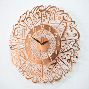 May include: A copper-colored wall clock with Arabic calligraphy around the edge. The clock face has a geometric design and Roman numerals.