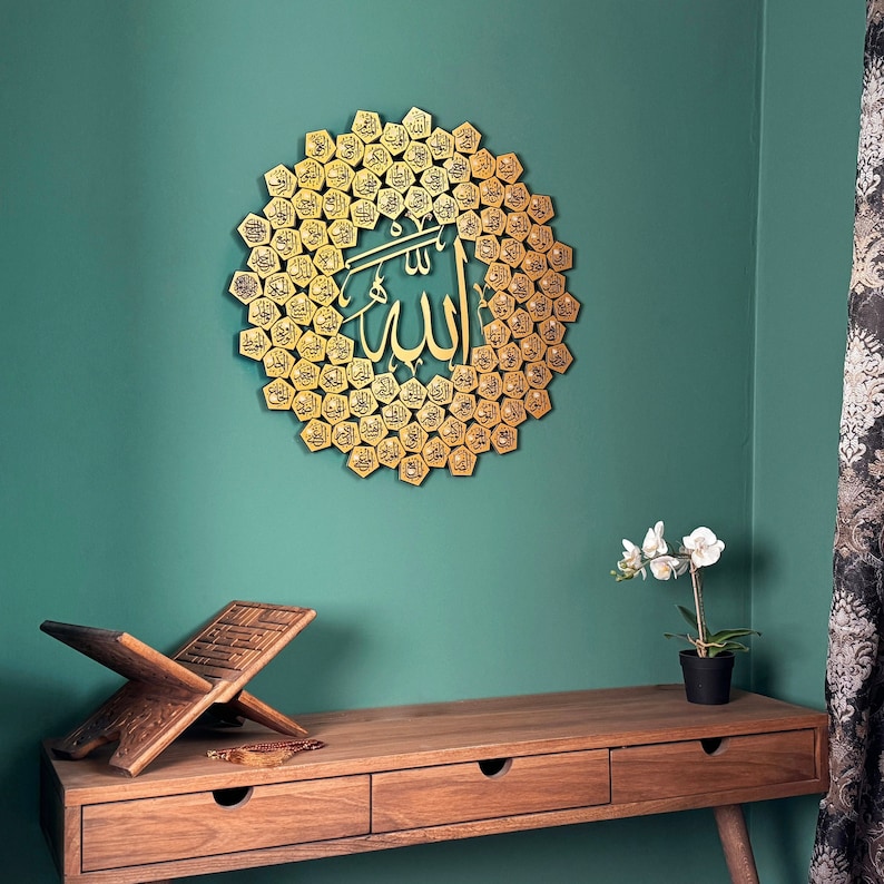 Peut inclure: Une d&eacute;coration murale en m&eacute;tal dor&eacute; repr&eacute;sentant le mot arabe &laquo;&nbsp;Allah&nbsp;&raquo; entour&eacute; d'un motif circulaire de petits hexagones. La d&eacute;coration est fix&eacute;e sur un mur vert sarcelle au-dessus d'une table en bois &agrave; deux tiroirs.