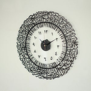 May include: A black clock with Arabic calligraphy around the face. The clock face is white with black numbers and hands.