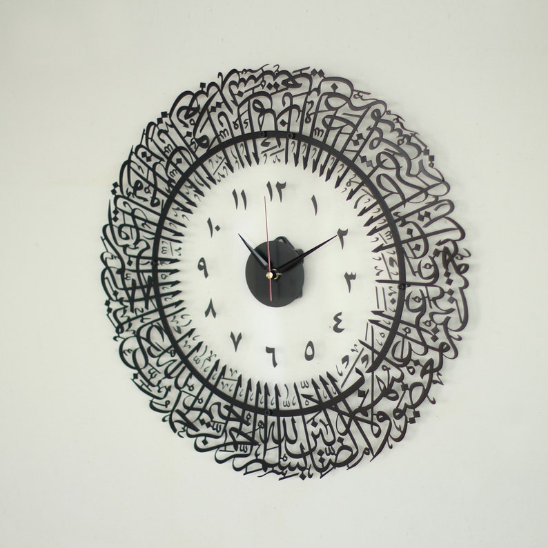 May include: A black clock with Arabic calligraphy around the face. The clock face is white with black numbers and hands.