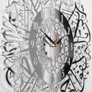 May include: A silver mirrored clock with Arabic numerals and a decorative design. The clock face features a geometric pattern and the hands are black and red.