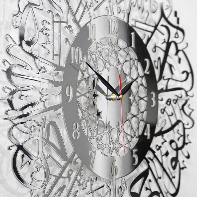 May include: A silver mirrored clock with Arabic numerals and a decorative design. The clock face features a geometric pattern and the hands are black and red.