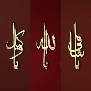 May include: Three gold-colored Arabic calligraphy wall art pieces. The pieces are mounted on a dark red background. The calligraphy is in a flowing script style, with each piece featuring a different design.