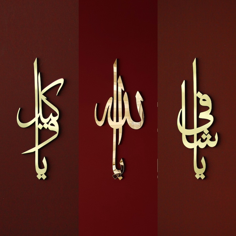 May include: Three gold-colored Arabic calligraphy wall art pieces. The pieces are mounted on a dark red background. The calligraphy is in a flowing script style, with each piece featuring a different design.