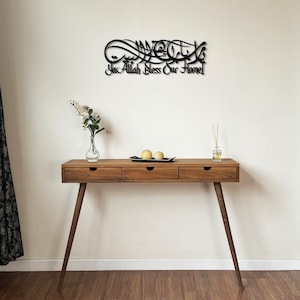 May include: A wooden console table with three drawers and tapered legs. The table is decorated with a black metal wall art featuring Arabic calligraphy that reads "Ya Allah Bless Our Home".