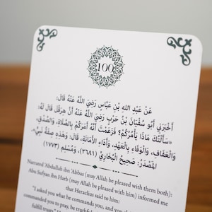 K&ouml;nnte beinhalten: Eine wei&szlig;e Karte mit arabischem Text und einem dekorativen Rand. Die Karte zeigt ein kreisf&ouml;rmiges Design mit der Zahl 100. Der Text ist in Schwarz und enth&auml;lt arabische Schriftzeichen und eine englische &Uuml;bersetzung.
