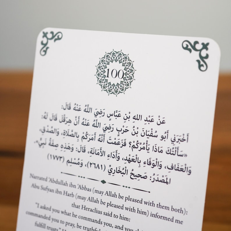 K&ouml;nnte beinhalten: Eine wei&szlig;e Karte mit arabischem Text und einem dekorativen Rand. Die Karte zeigt ein kreisf&ouml;rmiges Design mit der Zahl 100. Der Text ist in Schwarz und enth&auml;lt arabische Schriftzeichen und eine englische &Uuml;bersetzung.