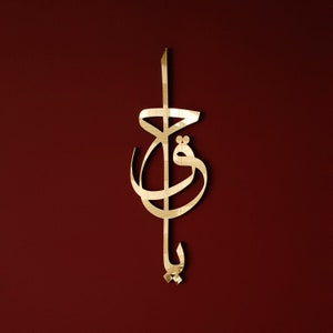 May include: Gold-coloured metal wall art featuring a stylised Arabic calligraphy design. The design is intricate and features flowing lines and curves.