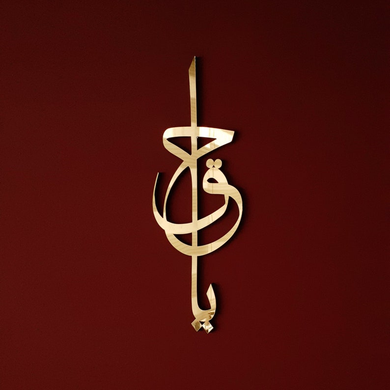 May include: Gold-coloured metal wall art featuring a stylised Arabic calligraphy design. The design is intricate and features flowing lines and curves.