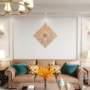 May include: A decorative wall clock with a diamond-shaped design and intricate cut-out patterns. The clock is made of a copper-colored metal and features a central clock face with hands. The clock hangs above a brown leather sofa with teal and patterned pillows.